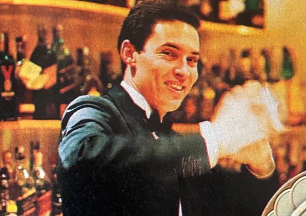Celio Alves de Freitas posa em frente ao bar enquanto prepara um drinque usando a coqueteleira