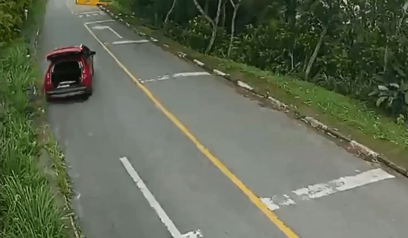 A imagem mostra um carro vermelho, em uma estrada, com o porta-malas aberto e em movimento.