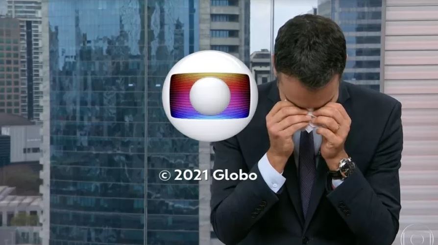 cesar tralli ao vivo no estúdio com a cabeça abaixada levando um lenço aos olhos para secar suas lágrimas enquanto o símbolo da globo aparece na tela, ao final dos créditos
