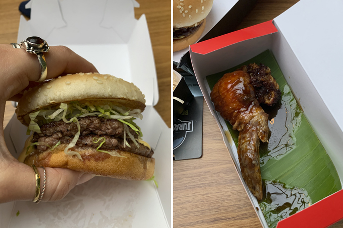 Jurassic Park Burger Restaurant Duas imagens verticais unidas por linha fina. À esquerda, mão segurando hambúrguer duplo com alface e pão com gergelim sobre caixinha branca de papelão. À direita, caixa retangular com asinha de frango sobre folha de bananeira em cima de mesa de madeira.