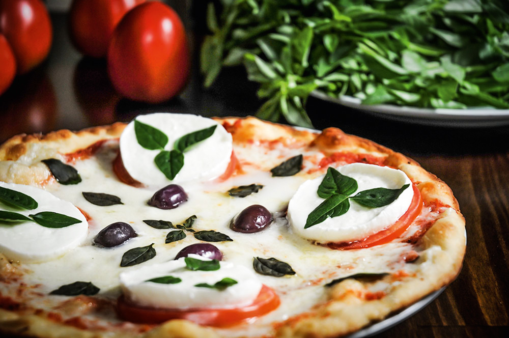 Pizza caprese da pizzaria Sala Vip preparada com rodelas de tomate-caqui e de muçarela de búfala, folhas de manjericão fresco e azeitona preta