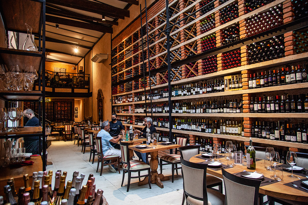 Ambiente interno do restaurante decorado por uma parede repleta de garrafas de vinho