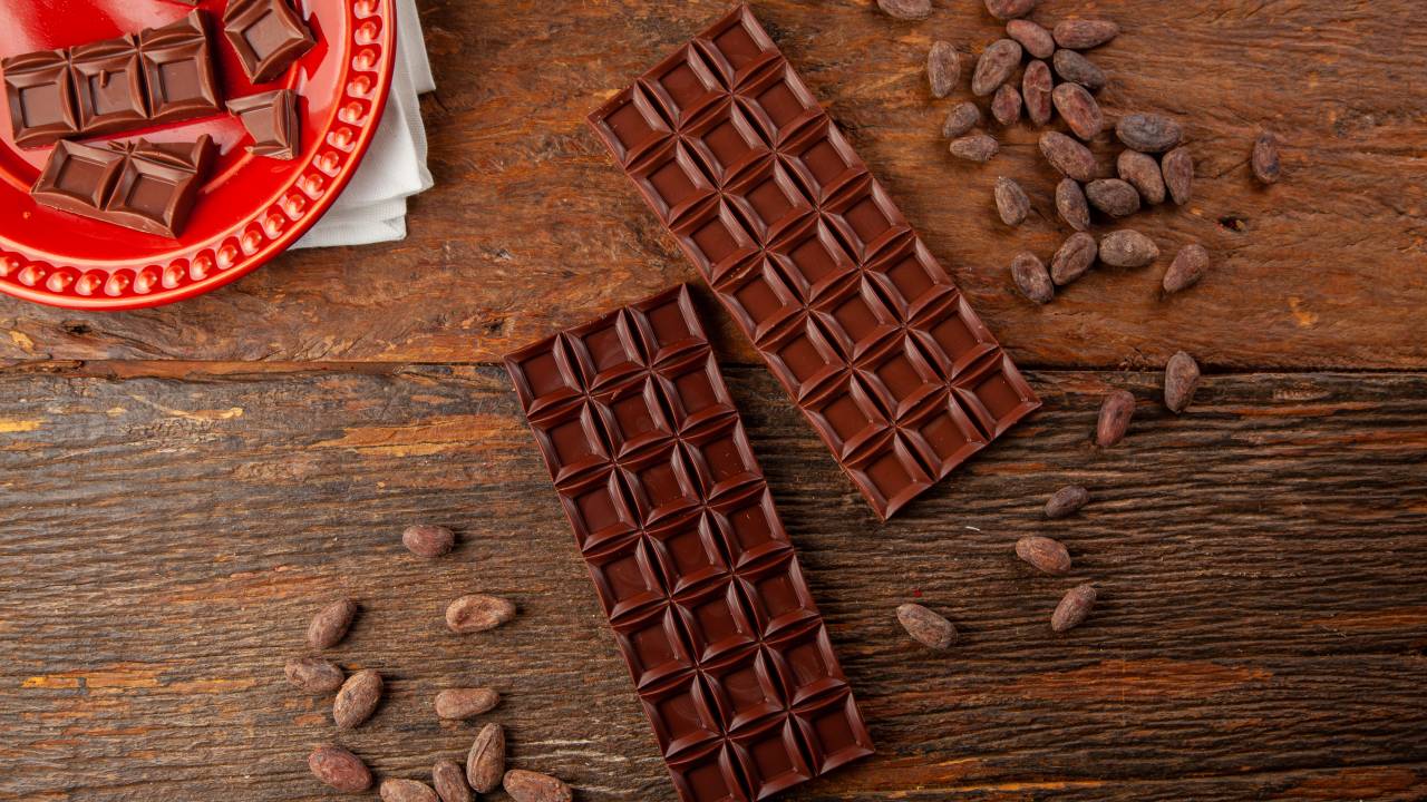 Barras de chocolates ao lado de pepitas sobre mesa de madeira.