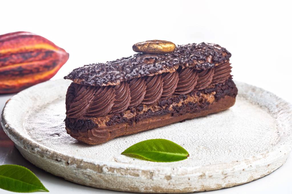 Chocolate Week – Casarìa Éclair de chocolate sobre prato de pedra branca com recheio de chocolate.