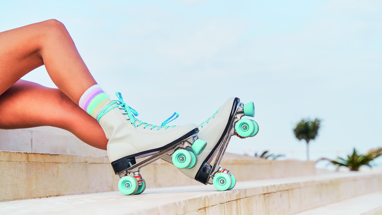 Foto mostrando duas pernas com patins brancos de rodas verdes deitados em uma escadaria branca, com um céu azul limpo ao fundo.