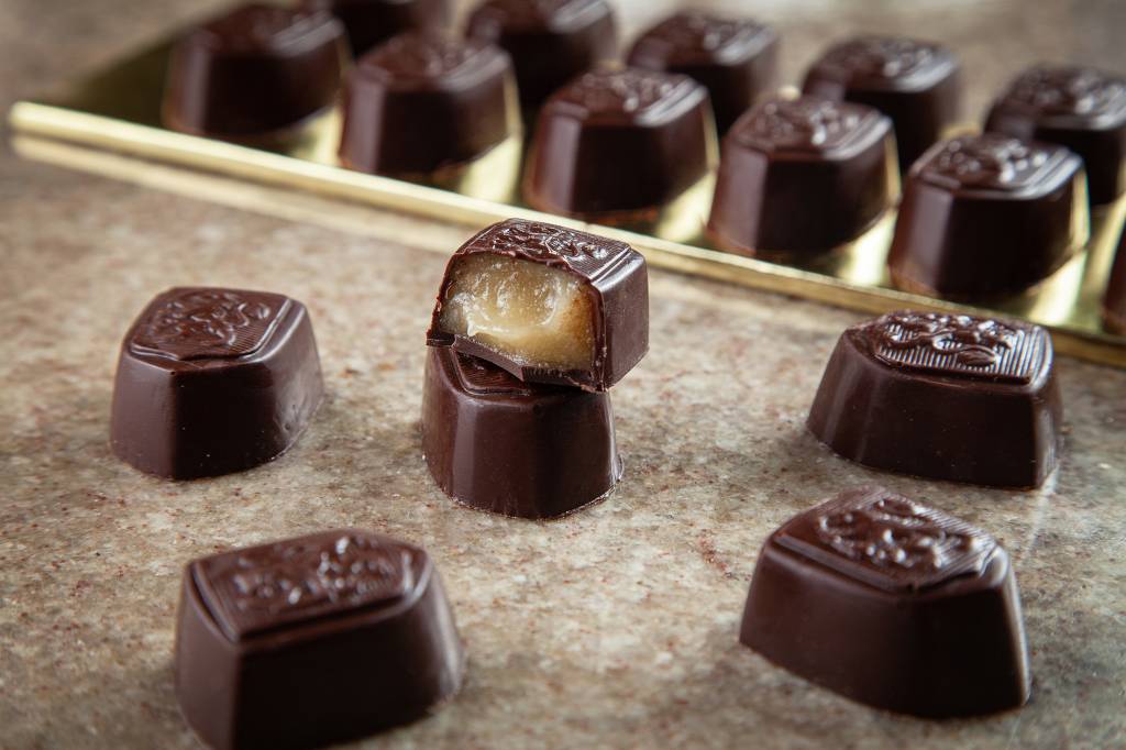 Achados ELO – Chocolates Marghi Bombons de chocolate sobre mesa de pedra com um deles cortado ao meio de recheio branco.