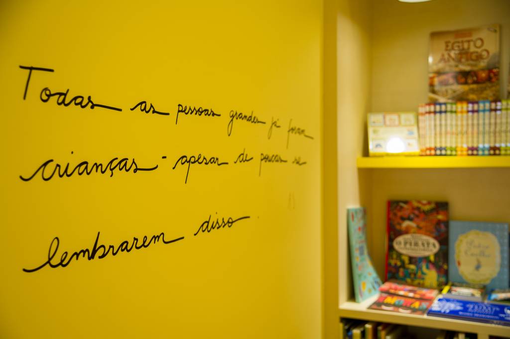 Livraria do Brooklin (Rogério Pallatta) Foto em detalhe exibe frase escrita em uma parede branca. À direita, alguns livros em prateleiras.