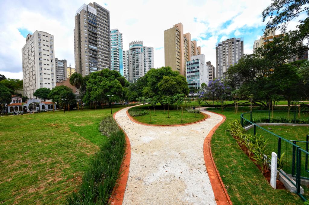 Parque Augusta (Alexandre Battibugli) (6) Via com chão branco aparece no meio de um gramado com prédios no horizonte.