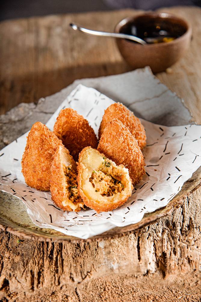 Tujuína Porção de seis unidades de coxinha recheadas de frango servidas sobre peça de cerâmica