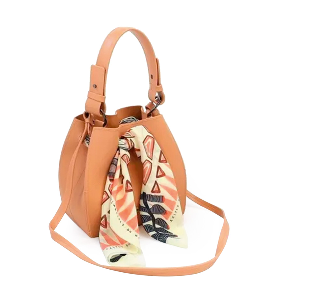 colcci.png Uma bolsa em formato oval é bege e tem um lenço pendurado na frente com estampa floral
