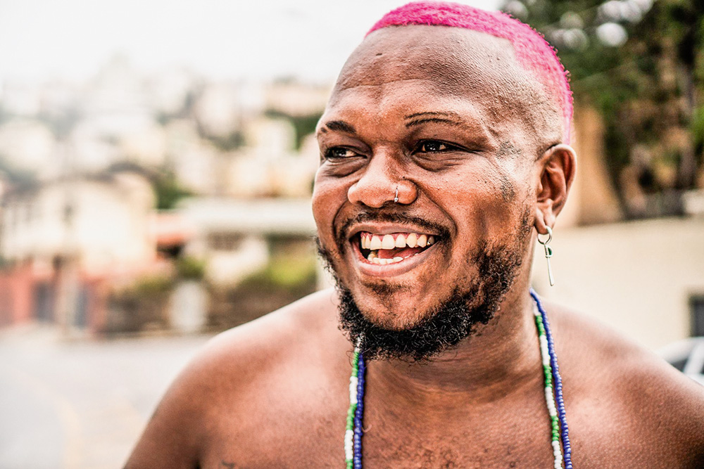 A imagem mostra o rapper Djonga, sem camisa, sorrindo.