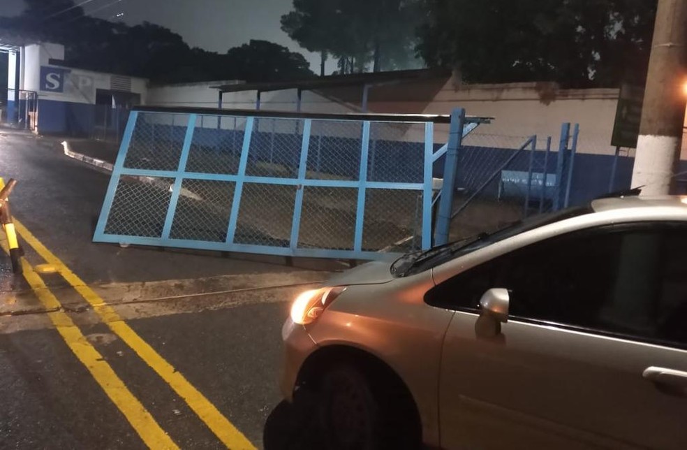 Imagem mostra carro parado e, à frente, portão parcialmente destruído