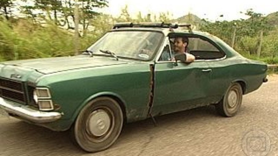 Imagem mostra um Opala antigo verde escuro com um homem dirigindo