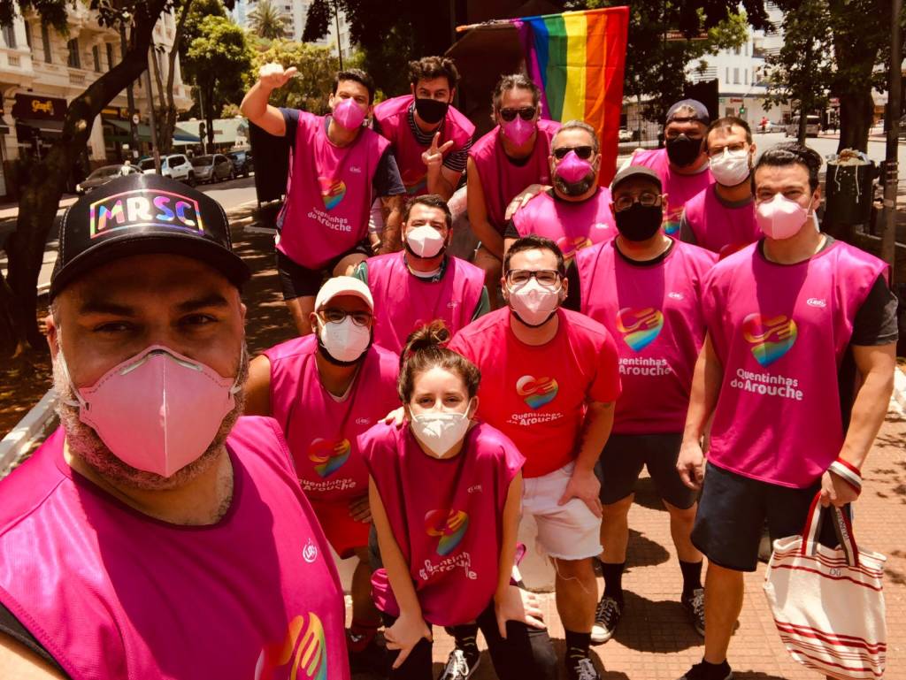 0a7431bb-ab6e-4880-b541-90599a818e22 Voluntários do projeto tiram selfie. Eles trajam coletes cor-de-rosa e levam consigo uma bandeira LBGT.