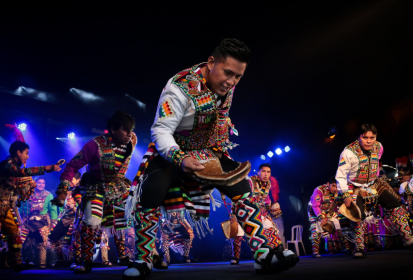 Foto de dançarinos no palco. Eles usam roupas típicas e coloridas.