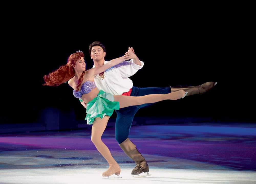 Em uma apresentação, um casal vestido de A Pequena Sereia e o príncipe está dançando sobre patins no gelo