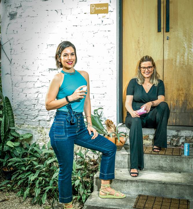 Imagem mostra duas mulheres, uma em pé, com um dos pés em uma escada. A outra, sentada na escada.