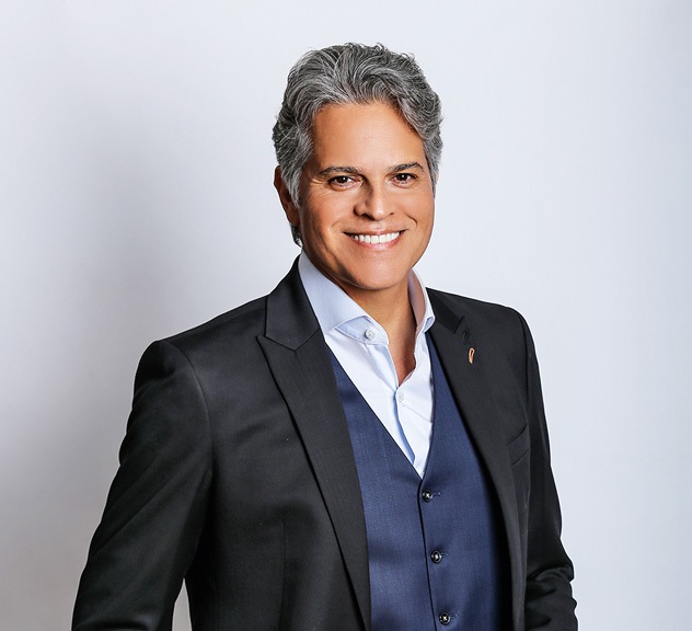 Juan Alba sorry para a câmera vestindo terno preto com colete azul. Tem cabelos grisalhos.