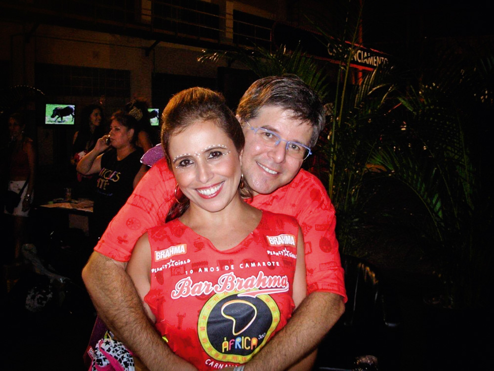 WhatsApp Image 2021-11-25 at 3.21.49 PM.jpeg (1) Imagem mostra um homem abraçando uma mulher por trás. Os dois vestem camisetas vermelhas.