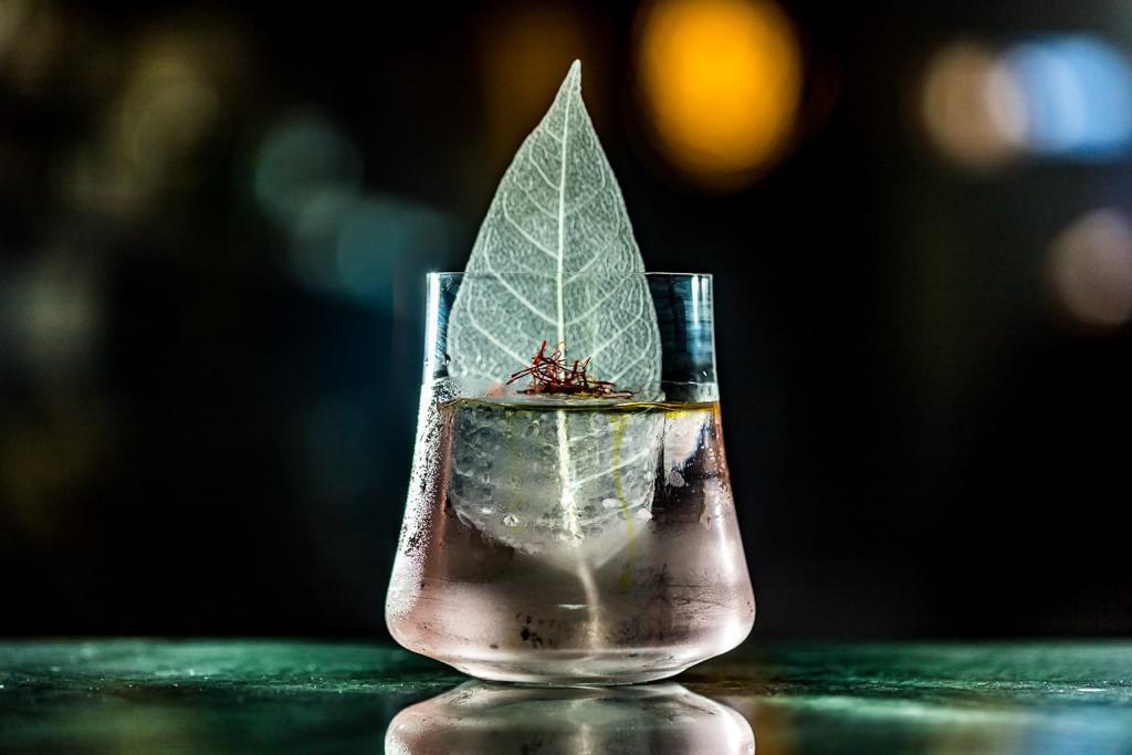 Boato Bar Drinque quase transparente servido em um pequeno copo de fundo redondo decorado por uma folha verde