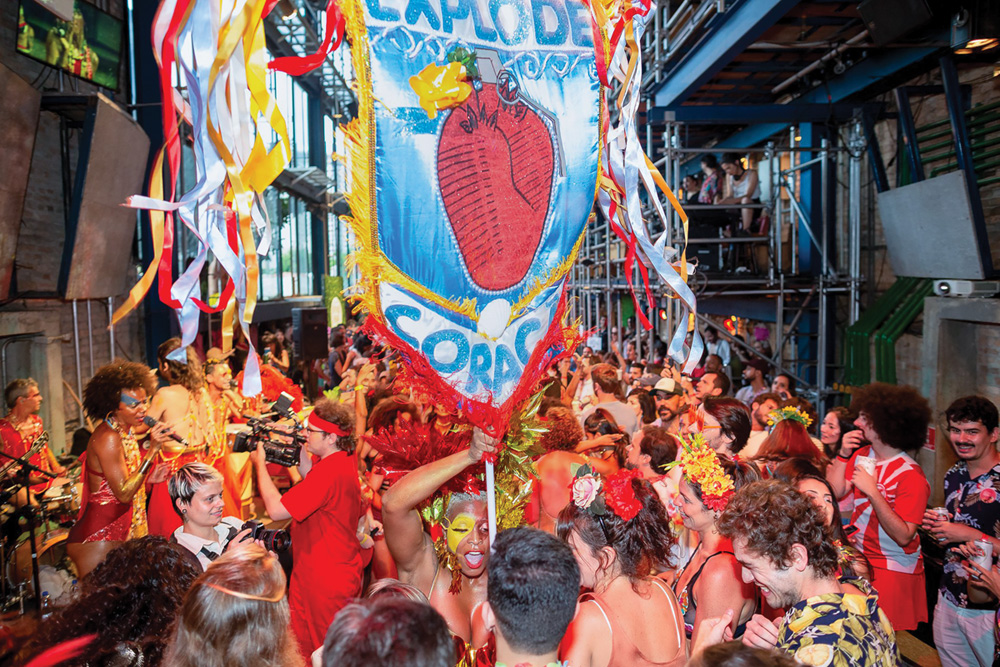 Imagem mostra aglomeração de pessoas com roupas vermelhas e uma bandeira ao meio, escrita "Explode Coração".