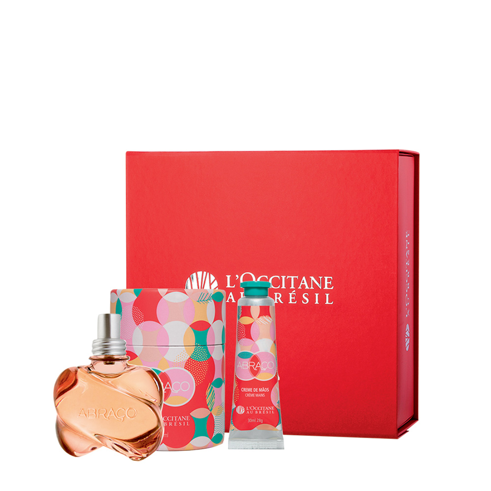 Kit com uma col&ocirc;nia e um creme. A caixa &eacute; vermelha e tem o nome da marca em dourado. Embalagens dos cosm&eacute;ticos s&atilde;o coloridas, em vermelho, rosa e azul.