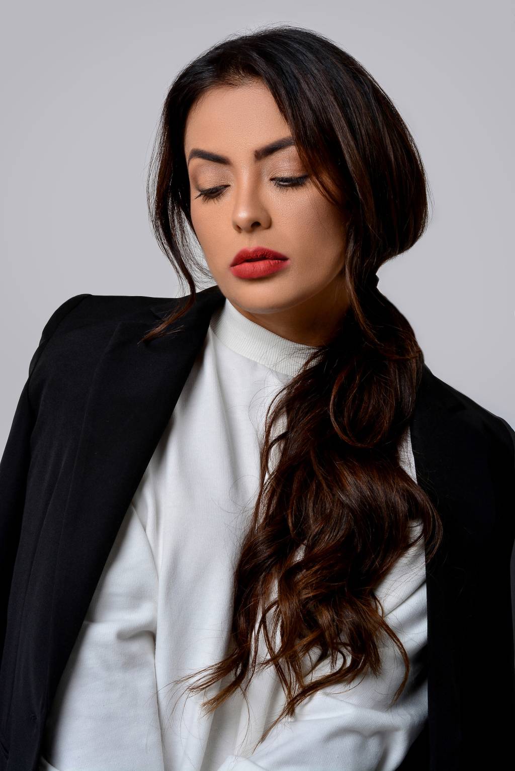 Li Martins, ex-integrante do grupo Rouge (Divulgação) Li Martins, ex-integrante do grupo Rouge, posa olhando para baixo. Veste blazer preto e blusa branca, com batom vermelho e cabelo longo preso, acomodado em um dos ombros.