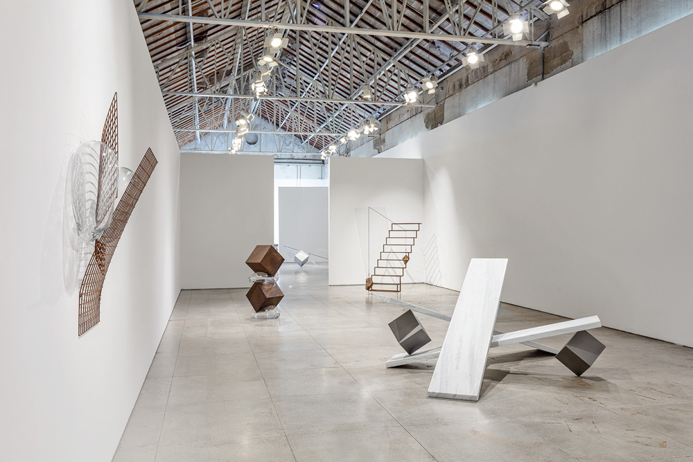 Peso 3-Créditos_Filipe Berndt.jpg Foto de uma ampla sala de galeria, onde estão dispostas, no chão e nas paredes, esculturas em formas geométricas. Uma delas, feita em material na cor branca, lembra uma gangorra. Outra, uma escada.