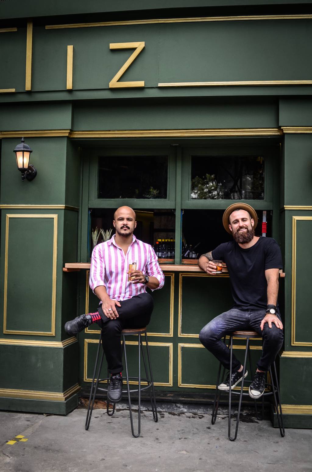 Liz Cocktails & Co Dois homens sentados em banquetas em frente a bar