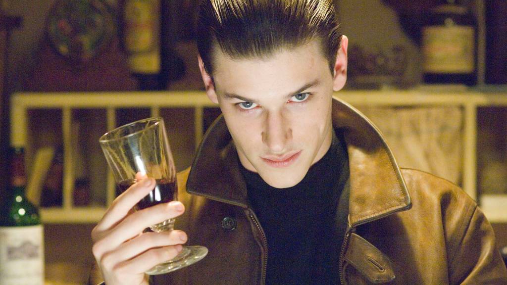 $value Imagem mostra um homem de jaqueta marrom, segurando um copo de vinho e olhando para a câmera.