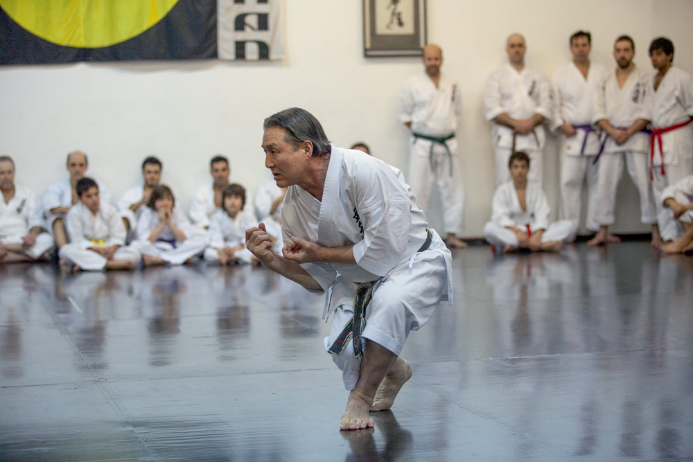 1.jpg Foto atual de Taketo na academia em Pinheiros. Ele está no centro e alguns alunos o observam encostados na parede.