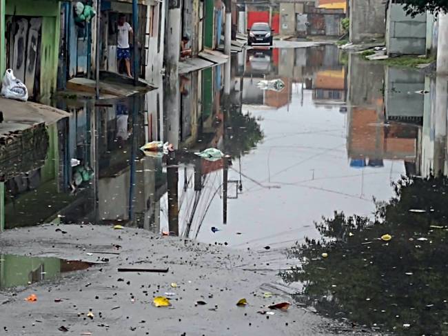 Imagem mostra rua completamente alagada. Um carro pode ser visto ao fundo, do outro lado do corpo d'água que tomou conta do asfalto.