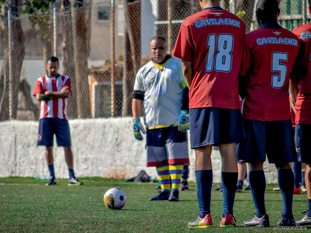 IMG_2500.jpg Imagem mostra homem com uniforme de goleiro e luvas preparando para bater uma falta. É possível ver alguns jogadores, à direita, enfileirados em uma barreira.