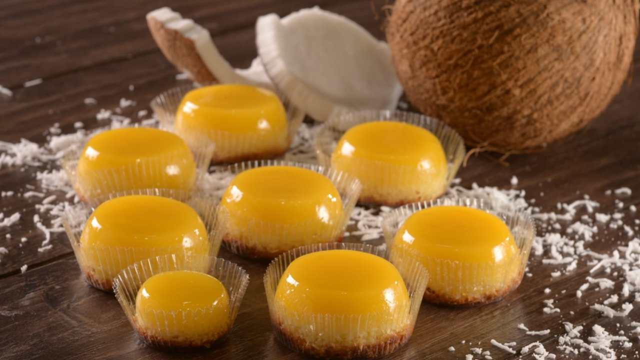 Sete quindins grandes e um pequeno quindim sobre mesa de madeira decorado por raspas de coco