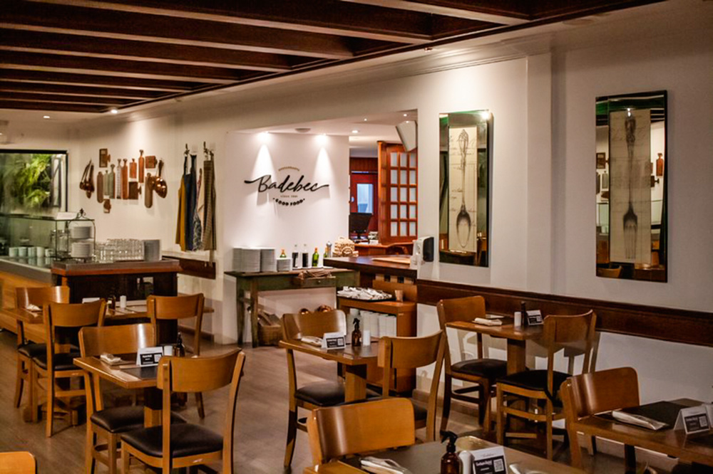 Ambiente de restaurante com mesas e cadeiras de madeira e paredes brancas
