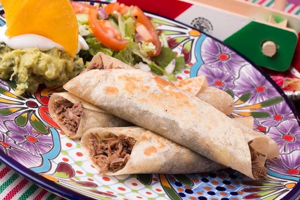 burritos Um prato clorido com três burritos de carne desfiada em cima.