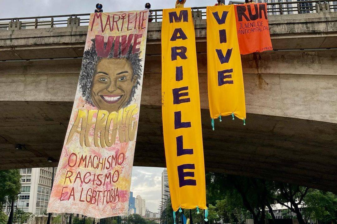 A foto mostra faixs estendidas no cenro de SP que lembram o assassinato de Marielle Franco e de Anderson Gomes