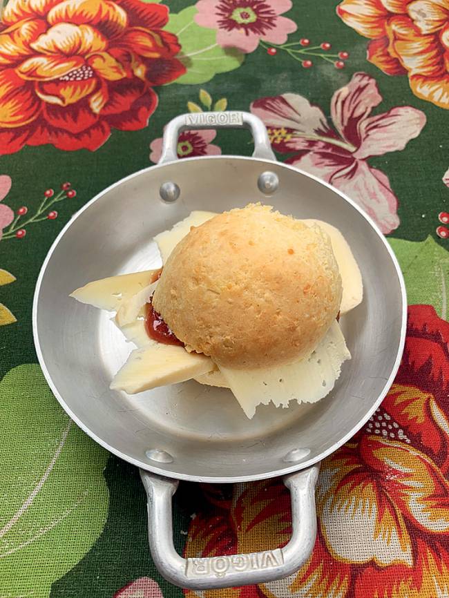 Pão de queijo servido em panelinha metálica e recheado por fatias de queijo e goiabada