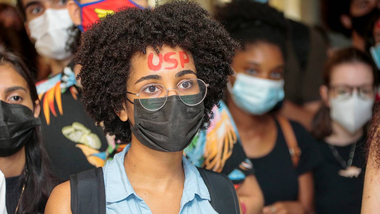 Imagem mostra aluna de óculos com a palavra USP escrita na testa