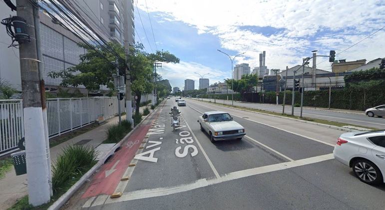 Imagem mostra avenida com ciclovia à esquerda e carro branco ao centro.