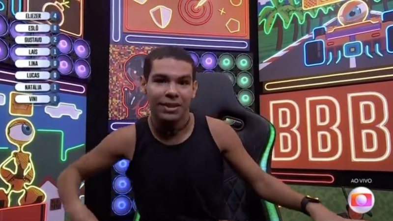 Imagem mostra Vyni se sentando em cadeira diante de câmera, inclinado para o lado após se desequilibrar