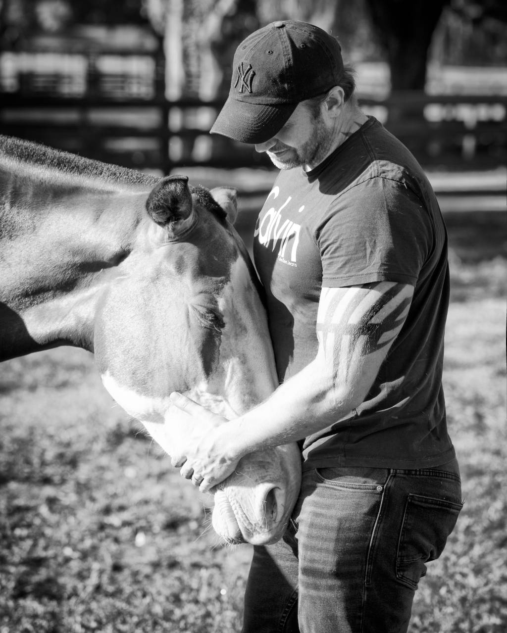 Raphael Macek (Arquivo Pessoal) Raphael Macek, fotógrafo especializado em cavalos, interage com cavalo no meio de um gramado. Veste boné e polo. Foto em preto e branco.