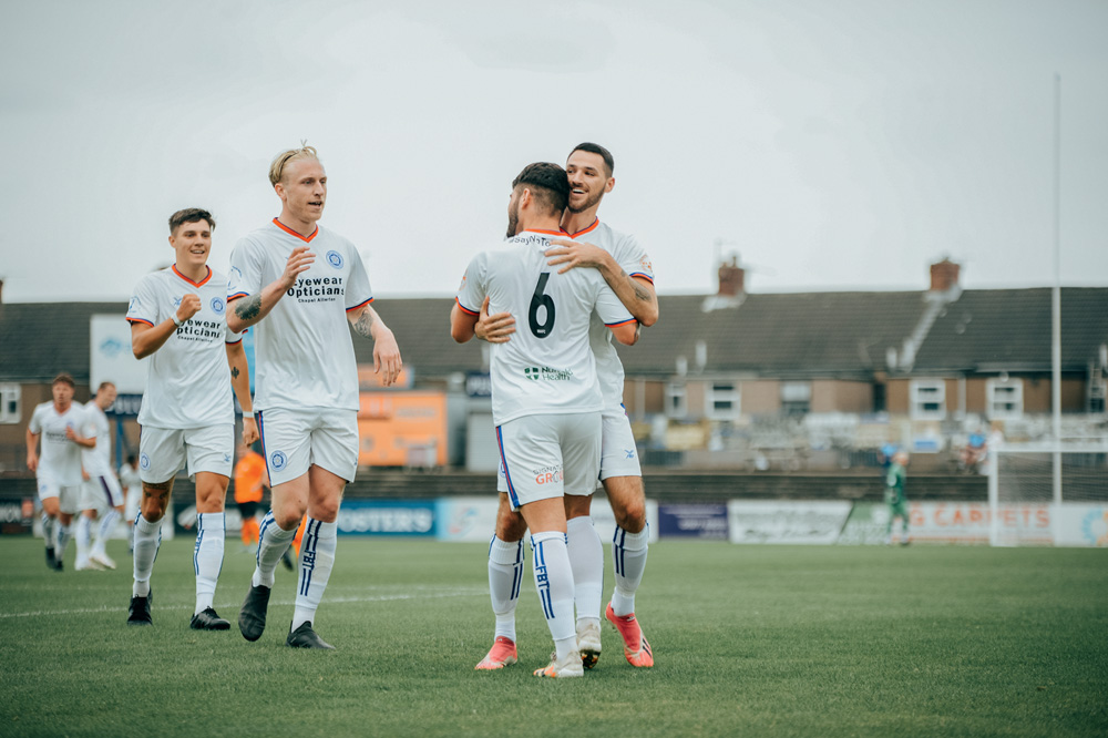 Wakefield A.F.C. Imagem mostra jogadores de futebol sorrindo e se abraçando. Eles vestem uniformes brancos