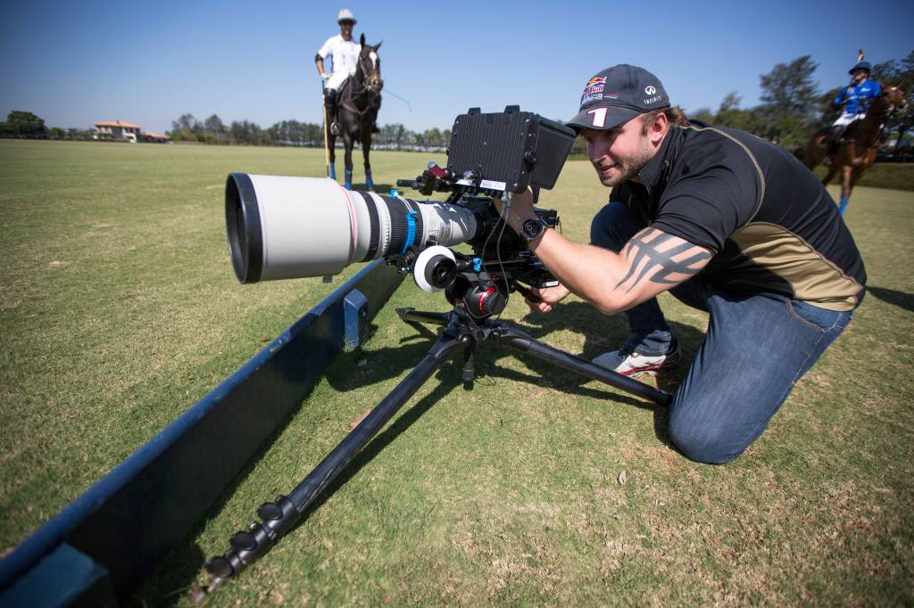Raphael Macek (Arquivo Pessoal) Raphael Macek, fotógrafo especializado em cavalos, posa de joelhos com câmera instalada em gramado.