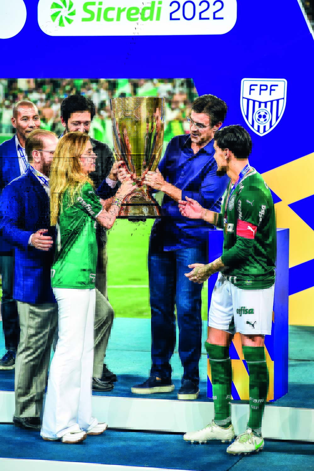 RODRIGOGARCIA_2.JPG Imagem mostra várias pessoas segurando um troféu dourado. Em destaque, um homem de camisa azul e calça jeans, sorrindo com as mãos na taça.