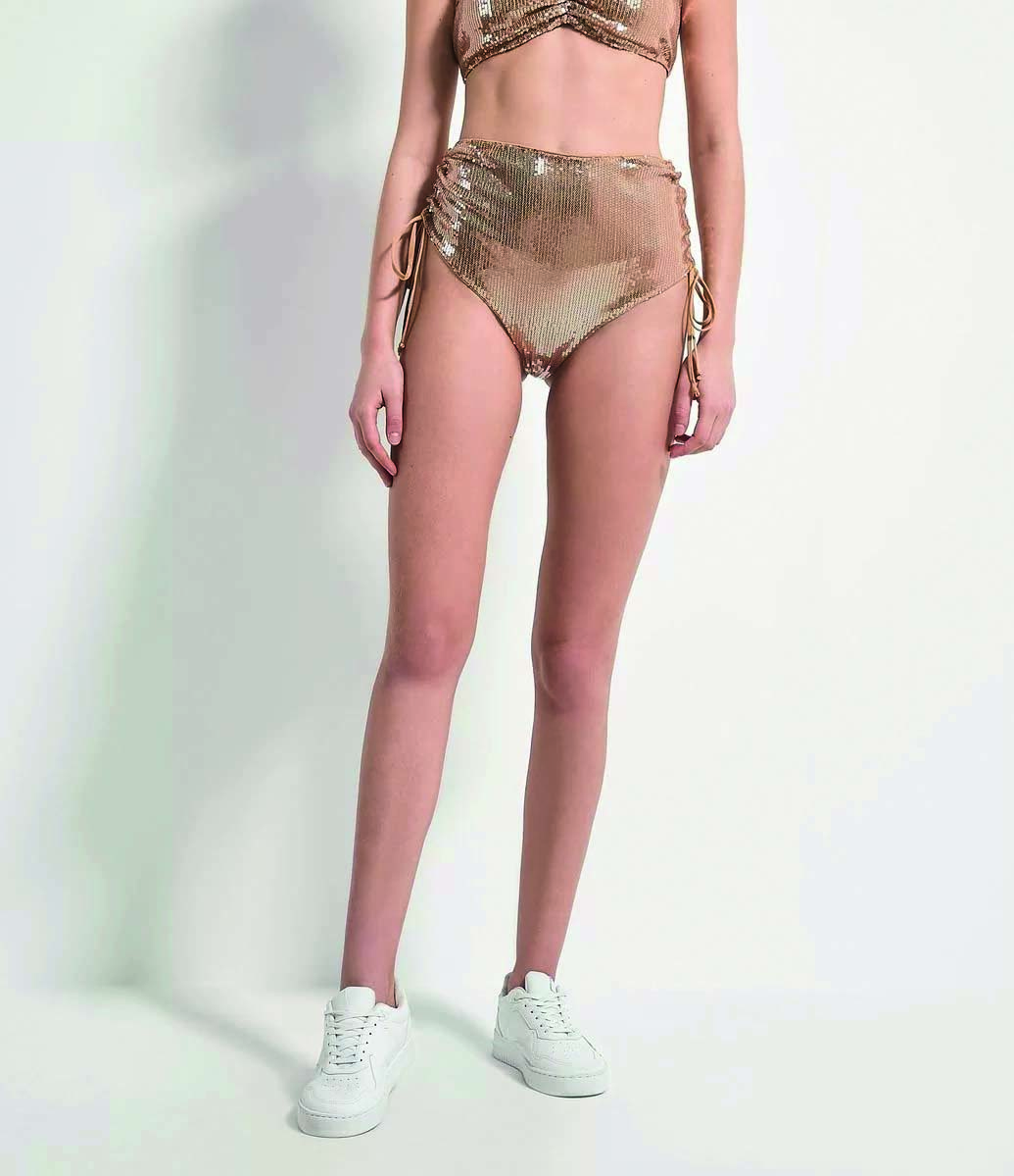 Modelo branca e magra usa um short de paet&ecirc; dourado e cavado