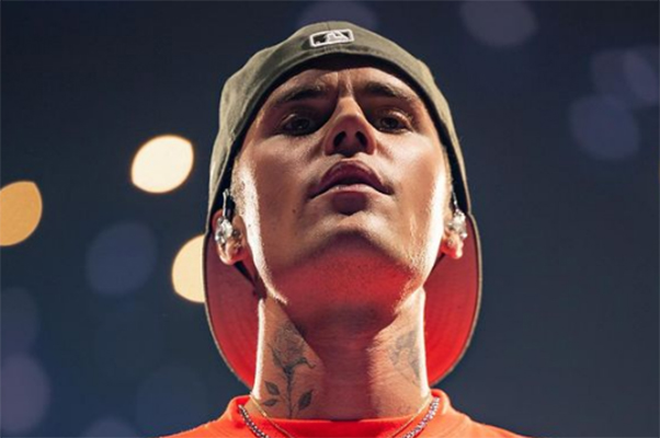 Imagem mostra Justin no palco, usando boné e blusa