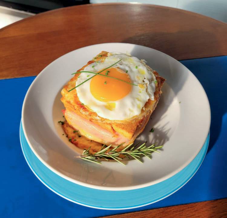 Croque madame com um ovo frito no topo e servido em prato de cerâmica de cor azul
