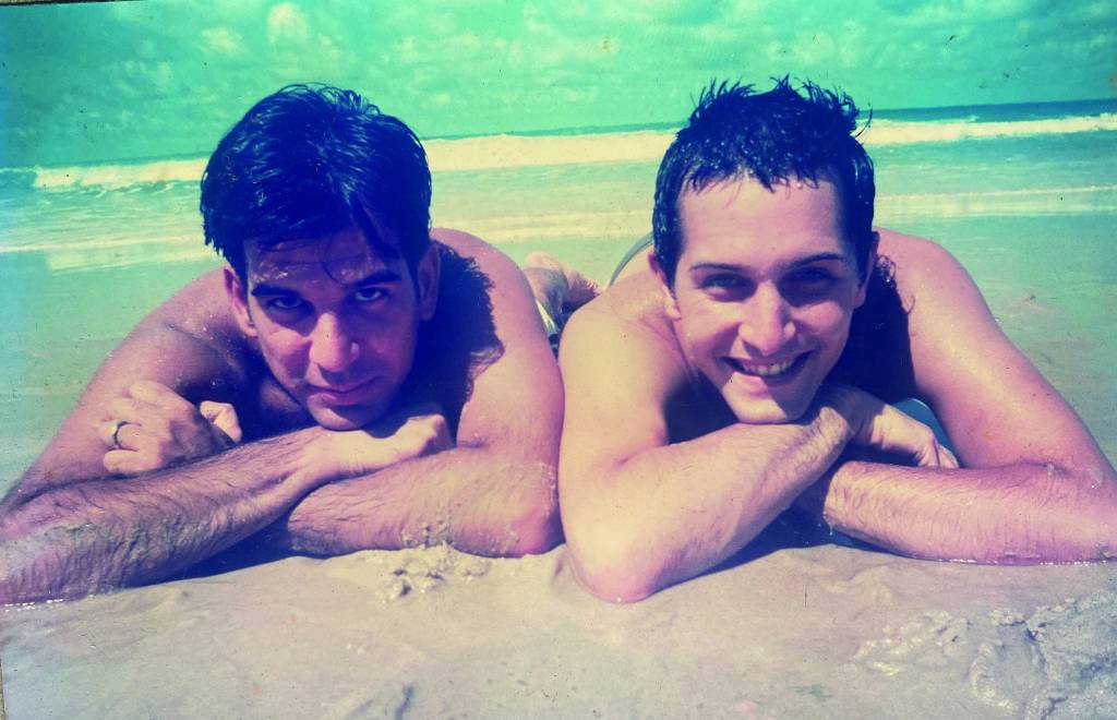 arlindo e fábio Fábio e Arlindo deitados na areia da praia posam um ao lado do outro para a foto, com a cabeça apoiada nos braços cruzados