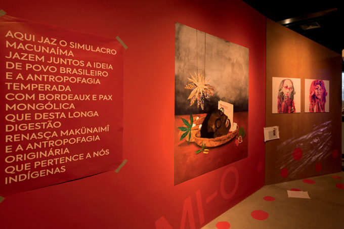 Imagem mostra sala com parede vermelha com uma pintura e um cartaz com um manifesto
